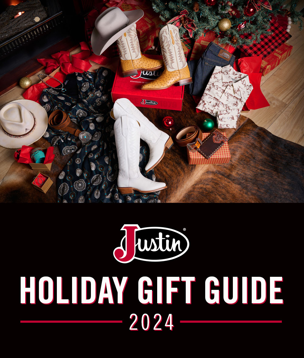 Justin Logo. Holiday Gift Guide 2024. Pasco 13” tan smooth ostrich boots, a hat, cream snap shirt, unwashed blue straight-leg jeans, and Evelyn Vintage Ivory 15” cowhide boots, under a Christmas tree.